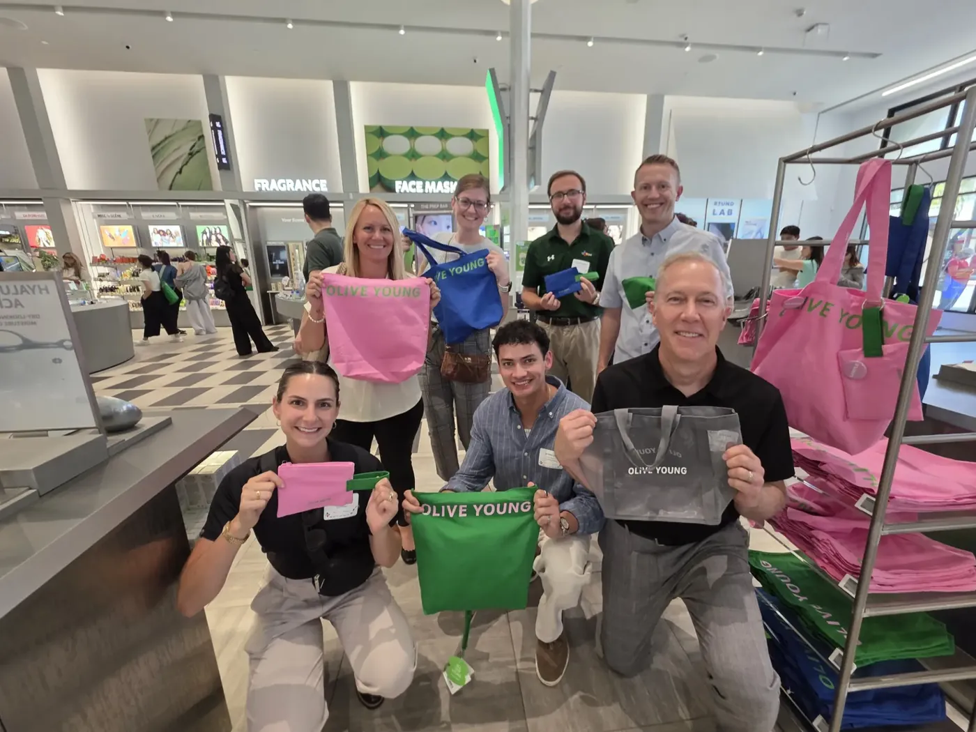 CJ America colleagues holding up branded tote bags and pouches together at the end of a checkpoint.