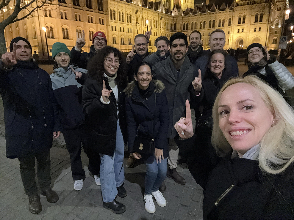 A team celebrating together outside a floodlit city landmark at night during a scavenger hunt.