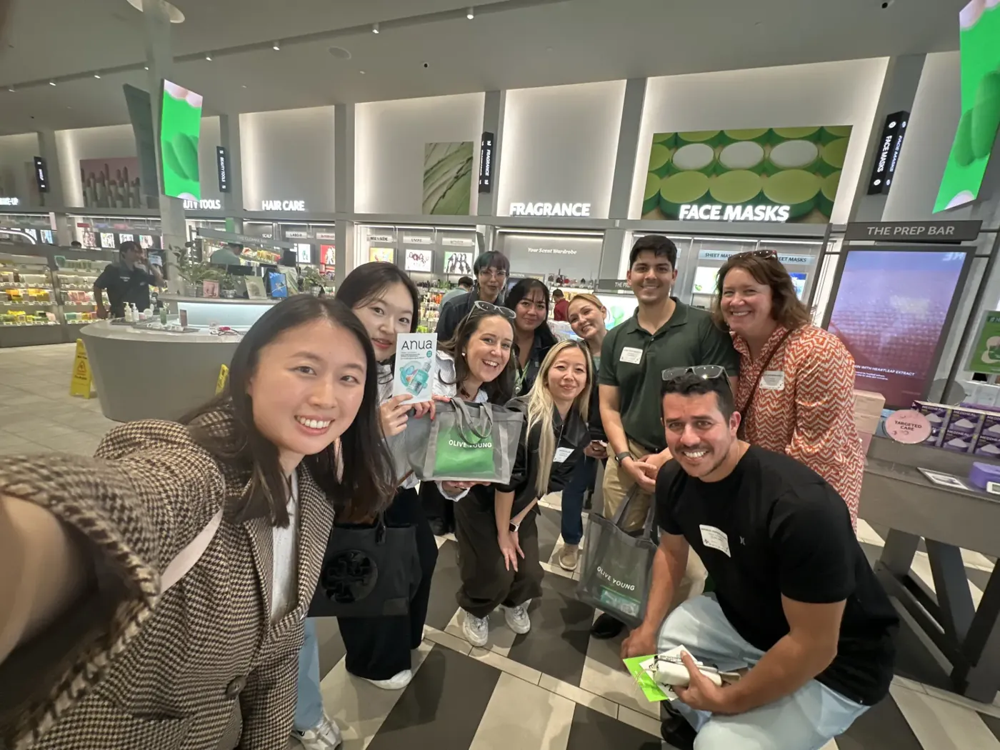 A CJ America team taking a group selfie inside an Olive Young beauty store during the ReadySet scavenger hunt.