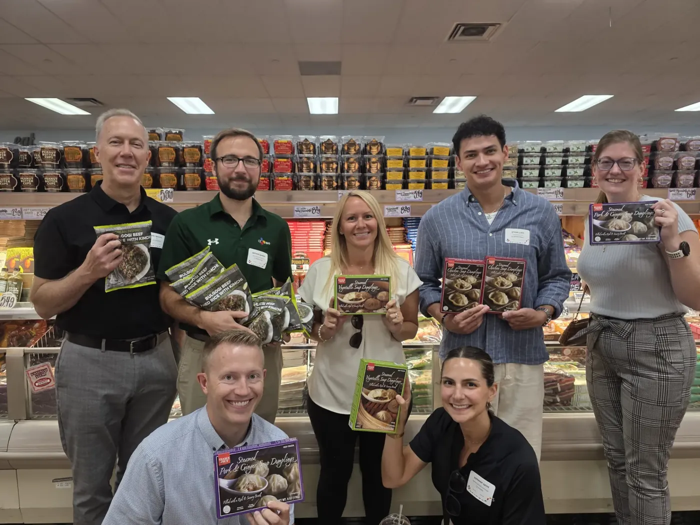 CJ America colleagues holding CJ food products together in the aisle of a grocery store during the scavenger hunt.