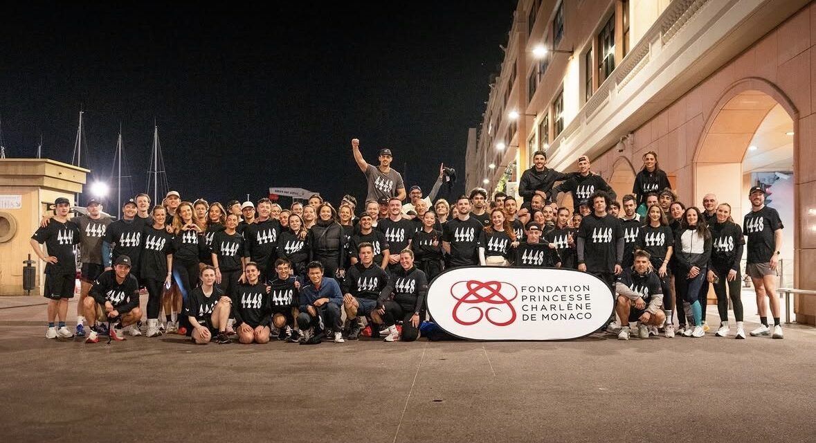 Runners in matching 4x4x48 shirts gathered at night beside the Fondation Princesse Charlène banner in Monaco.